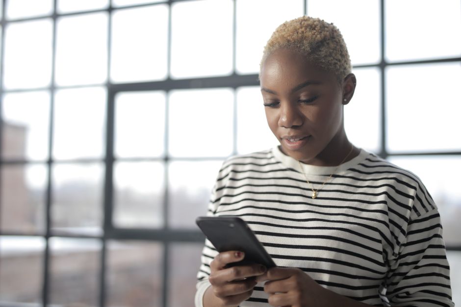 Young African American woman texting on smartphone by a window with natural light.